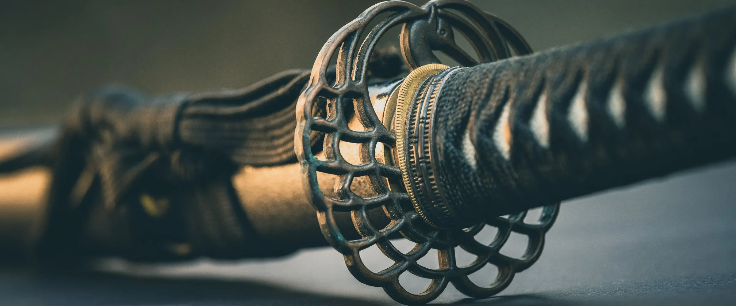 Close-up of a katana's hand guard and wrapped grip, lit from the side.